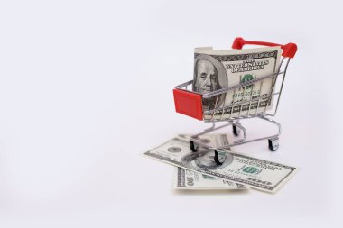 Beyaz arka planda el arabasında 100 dolarlık banknotlar. Süpermarket alışveriş konsepti, kara cuma ve siber pazartesi. Mağaza içi alımlar ve satış hazırlıkları için harcamalar. Metin için boş alan