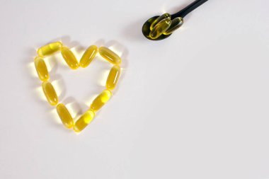 Kapsüllerdeki balık yağı kalp şeklinde beyaz bir zemin üzerinde. Kaşıkta balık yağı kapsülleri. Metin için boş alan. İyi kalp fonksiyonları için yararlı bir gıda takviyesi.