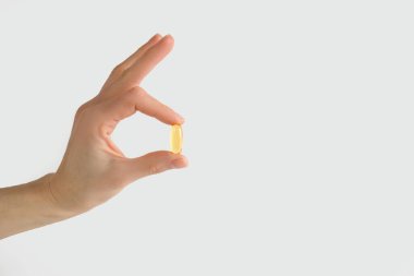 Bir adam balık yağlı bir kapsülü beyaz arka planda tutuyor. Metin için boş alan. Doktorun tavsiyesi, balık yağının kalp fonksiyonlarını geliştirmek için beslenme takviyesi olarak kullanılması.