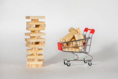 Beyaz arka planda tahta masa oyunu ve tahta bloklu küçük bir araba. Gayrimenkul inşaatı ve inşaat malzemeleri satın alma kavramı