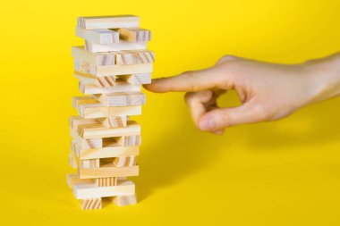 Sarı arka planda tahta masa oyunu. İnsanlar, dengenin önemli olduğu bir şans oyunu oynar. Tahta bloklardan yapılmış bir kule ve her seferinde bir parça koparan bir insan eli.