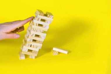 Sarı arka planda tahta masa oyunu. İnsanlar, dengenin önemli olduğu bir şans oyunu oynar. Tahta blok kulesi ağır eğildi ve çökmek üzere. Metin için boş alan