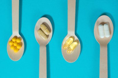 Mavi arka plan manzaralı tahta kaşıklarda vitaminler. Her gün için multivitamin seti. Vücudun işleyişini iyileştirmek ve sağlığın bozulmasını önlemek için bir vitamin kompleksi edinmenin önemi