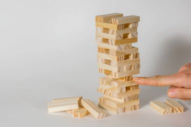 Beyaz arka planda tahta masa oyunu. İnsanlar, dengenin önemli olduğu bir şans oyunu oynar. Tahta bloklardan yapılmış bir kule ve bir insan eli Tim 'den bir parça koparıyor.