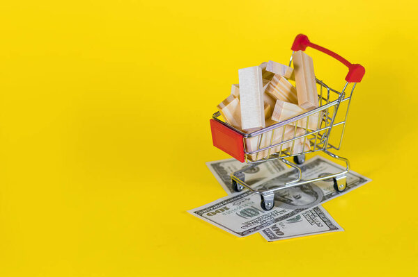 тележка с деревянными блоками и стодолларовыми купюрами на жёлтом фоне. концепция тратить деньги на строительство недвижимости. Свободное место для текста. красочные фото для социальных сетей