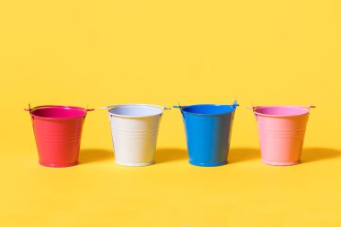 Sarı arka planda dört renkli oyuncak kovası. Beyaz mavi ve kırmızı kova bir sırada duruyor. Gelecekteki yenileme kavramı ya da hasat ya da ekin ekmeye başlama