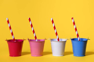 Sarı arka planda kırmızı ve beyaz pipetli dört kova. Kovalar kırmızı, beyaz, pembe ve mavi. Uçsuz bucaksız susuzluk ve sıcak bir günde suya ihtiyaç duyma kavramı. İçeceklerin orijinal servisi