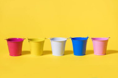 Sarı arka planda beş tane renkli oyuncak kovası. Beyaz mavi, pembe, sarı ve kırmızı kova yan yana duruyor. Gelecekteki yenileme kavramı ya da hasat ya da ekin ekmeye başlama