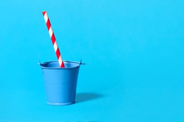 Açık mavi arka planda kırmızı ve beyaz çizgili pipetli bir oyuncak kovası. Standart olmayan içkilerle hafta sonu partisi konsepti. Metin için boş alan