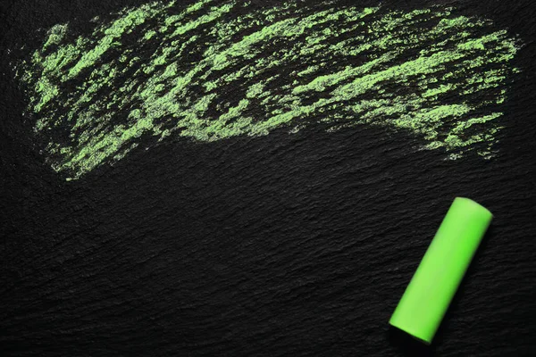 Green chalk on a black rough board. A simple image as a background with blank space for text and green chalk in the corner