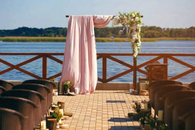 Nehir kıyısında gün batımına karşı süslenmiş bir düğün kemeri. Düğün günü ve düğün hazırlıkları için. Çiçekli güzel kemer, pembe kumaş ve konuklar için sandalyeler.