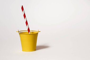 Beyaz arka planda şeritli kırmızı ve beyaz pipetli sarı oyuncak kovası. Hafta sonu parti konsepti. Standart olmayan içecekler ve susuzluk. Metin için boş alan