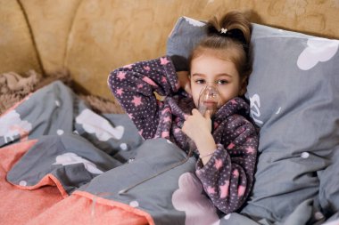 Küçük bir kız alerjisi var ve astım spreyi ile tedavi ediliyor. Çocuk öksürük için evde buhar spreyi ile tedavi edilir. Elleri yüzünün yanında astım spreyi tutan tatlı bir kız.