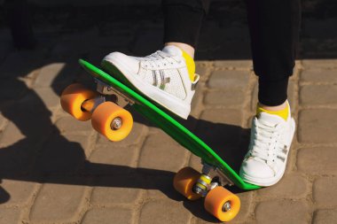 Beyaz spor ayakkabılı bir çocuk yeşil kaykay ya da pennyboard kullanıyor. Kız kaykayla numaralar yapmayı öğreniyor. Kaykay çok moda bir ulaşım aracı ve harika bir spor aracıdır.
