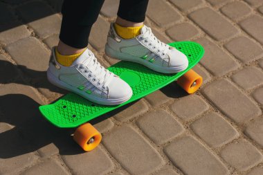 Tatildeki bir çocuk parkta yeşil bir kaykaya ya da pennyboard 'a biner. Açık hava sporlarının faydaları. Kaykay ve bacakları kapatın. Tüm vücut için spor.