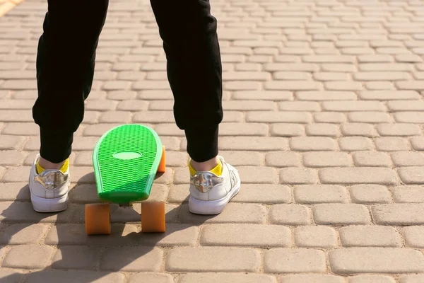 The girl is riding a skateboard in the park. The child is dressed in bright clothes and is learning to ride a green penny board or skateboard. Skateboarding is a great fitness activity