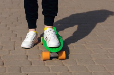 Parkta bir çocuk yeşil kaykay ya da bozuk para kaykayına biniyor. Açık hava sporlarının faydaları. Kaykay ve bacakların yakın görüntüsü