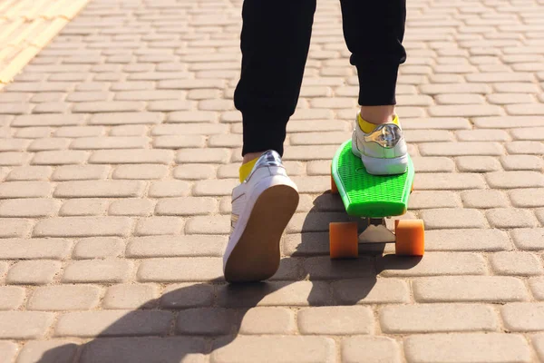 一个少年正在公园里骑绿色滑板或便士板 这孩子穿着鲜艳的衣服 喜欢滑板 滑板可以改善协调与平衡 — 图库照片