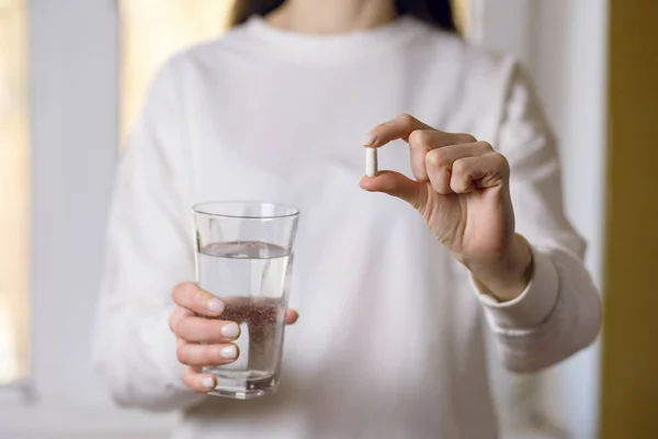 A woman holds a glass of water and a pill in her hands close-up. Health problems and treatment with pills or antibiotics. Concept of pain reliever or medicine to improve health