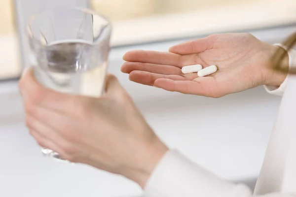 Bir kadın elinde bir bardak su ve bir hap tutuyor. Genç bir kadın hastalığı antibiyotiklerle tedavi ediyor. Baş ağrısı ya da karın ağrısı ilaçla hafifletilebilir. Metin için boş alan