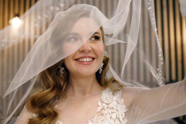 Genç bir gelin damat ile buluşmadan önce yüzünün bir kısmını peçeyle kapatıyor. Mutlu bir gelinin portresi Kendi düğün gününün tadını çıkarıyor