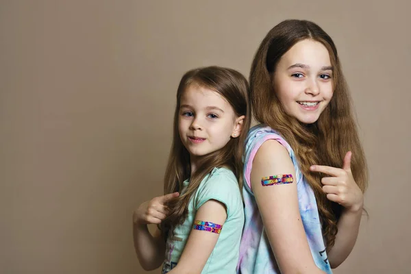 stock image Two girls vaccinated against coronavirus infection smile and point a finger at the vaccination site. A patch on the arm after being vaccinated against COVID-19 infection. Medicines fight infection