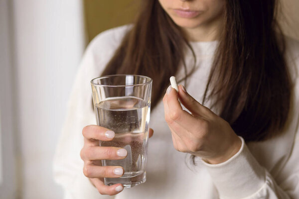 The woman is being treated, holding a glass of water and an anesthetic pill in her hand. A pill with a medicine or antibiotic to improve health. Home treatments and the importance of medicine