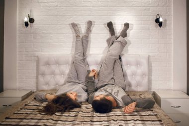 Genç bir heteroseksüel çift yatakta bacaklarını duvara dayamış ve birbirlerinin ellerini tutuyorlar. Sevgililer evde dinlenir. Güzel genç çift birlikte vakit geçiriyor.