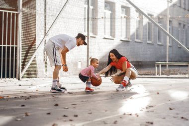 Atletik bir aile geceyi basketbol sahasında spor yaparak geçirir. Sepet topu tutan küçük bir kız. Genç ebeveynler spor kıyafetleri giyerler. Genç ve mutlu bir aile spor için geliyor.