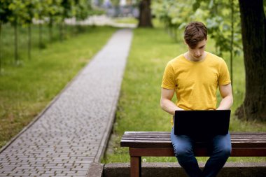 Bir öğrenci parkta bir bankta oturur ve dizüstü bilgisayar kullanır. Uzak serbest çalışma ya da modern teknolojiyi kullanan öğrencileri uzaktan öğrenme. Uzaktan kumandalı bir bilgisayar uzmanı. Metin için boş alan