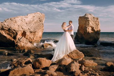 Gelin ve damat, deniz ve dağların arka planında sarılıp düğün günü taşın üzerinde dururlar. Gelin şık beyaz bir gelinlik giyiyor. Yeni evliler günbatımının tadını çıkarır.