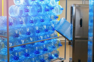 Drinking water plant and equipment for the purification and processing of plastic. Stand filled with blue plastic bottles. Automatic cleaning and filling of drinking water clipart
