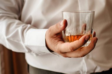 Elinde bir bardak viski olan beyaz gömlekli bir adam. İşte yorucu bir günün ardından rahatlama. Konyak güçlü erkekler için elit bir alkoldür.