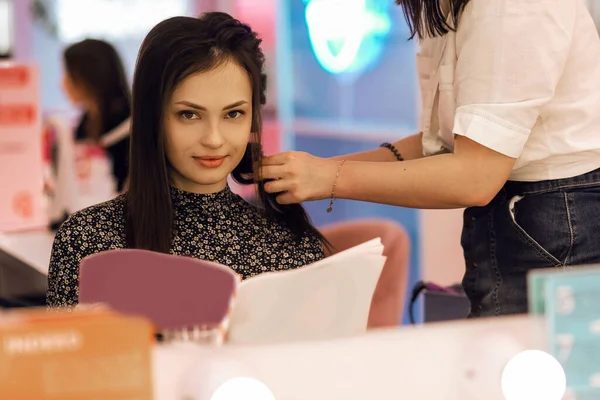 スタイリストは美容室で若いブルネットのためのヘアスタイルを作成します スタイリッシュな髪型を作成する過程で プロの美容師は美しい女性の髪を編みます — ストック写真