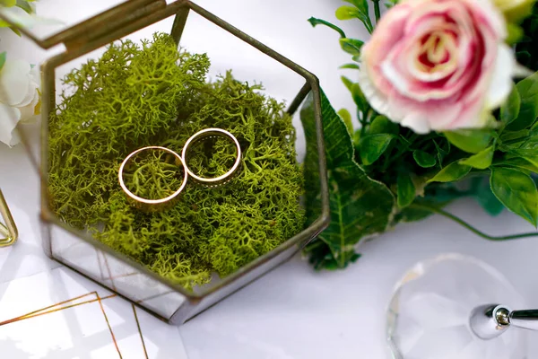 新郎和新娘的金婚戒指躺在桌上的一个玻璃盒里举行婚礼 用鲜花装饰的特写结婚戒指 — 图库照片
