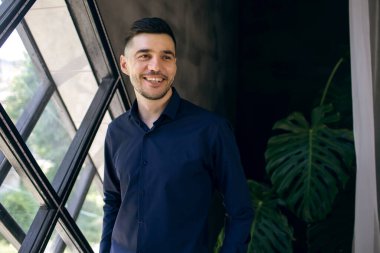 İçerideki pencerenin arka planında gülümseyen mutlu bir adamın portresi. Sakallı yakışıklı adam gülümsüyor ve başka tarafa bakıyor.