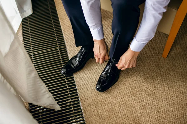 一个穿着白衬衫和连衣裙的男人在酒店房间里系上了专利皮鞋 时尚男人穿上鞋特写 为商务会议或婚礼做准备 — 图库照片