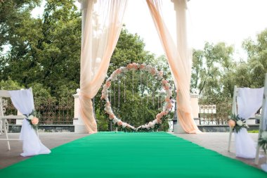 Gelin ve damat için yeşil halılı kristal kolyeli düğün kemeri. Geleneksel bir açık hava düğün töreni. Düğün töreni için mükemmel bir dekor.