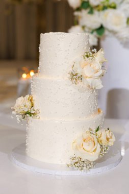 İnci ve narin güllerle süslenmiş üç katlı güzel bir düğün pastası ziyafette romantik bir dekorasyon yaratır. Nefis kremalı beyaz bir pasta izole bir şekilde duruyor.