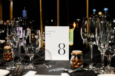 Minimalist masa numarası 8 olan zarif bir düğün masası, cam eşyalar, mumlar, şarap şişeleri ve küçük konuk içkileri. Sofistike siyah temalı olay dekoru
