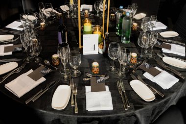 Cam eşyalar, çatal bıçaklar, mumlar ve yer kartlarıyla zarif bir karşılama masası. Siyah çarşaflar, şişe su, şarap ve küçük misafirlerin beğendiği sofistike bir etkinlik dekoru.