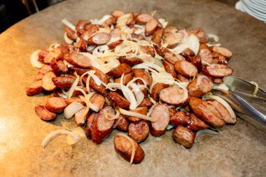 Izgara sosis dilimleri sıcak ızgarada sotelenmiş soğanla pişirilir. Sulu, kaşarlanmış et ve karamelli soğan sıcak, iştah açıcı tonları olan kırsal ve doyurucu bir yemek sunumu yaratır.