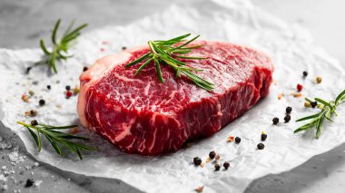 Mermerli çiğ biftek, biber, tuz ve parşömen kağıdında taze biberiye. Pişmemiş et, gurme yemek ya da ızgara için hazırlanmış, yakın çekim dokusu.