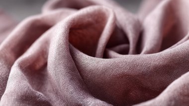 Yumuşak katlanmış kumaş gül renginde, dokunmuş dokuyu ve yumuşak örtüyü gösteriyor. Tasarım projeleri, kumaş arkaplanları ve malzeme örnekleri için tekstil detaylarının yakın plan çizimi ideal