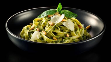 Fesleğen soslu taze tagliatelle, çam fıstığı ve tıraş edilmiş parmesan siyah bir kasede koyu bir arka planda, canlı renkte, zengin dokuda ve gurme sunumunda servis edilir.