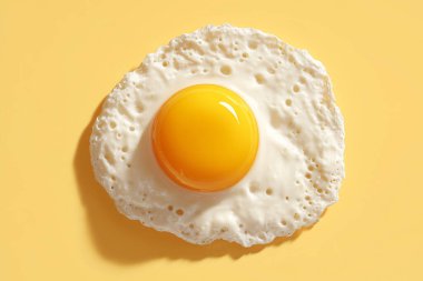 Parlak sarı sarısı ve desenli yumurta beyazından oluşan sade sarı arkaplana yerleştirilmiş yumurta, temiz ve canlı bir sunum için.