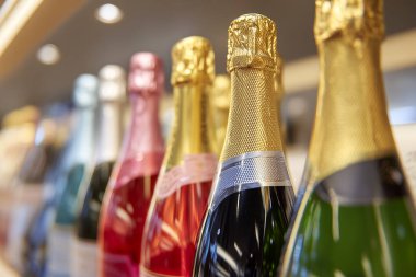 Çağdaş bir perakende ortamda rafa konmuş parlak folyo kapaklı şarap şişeleri koleksiyonu, farklı çeşitleri vurguluyor.