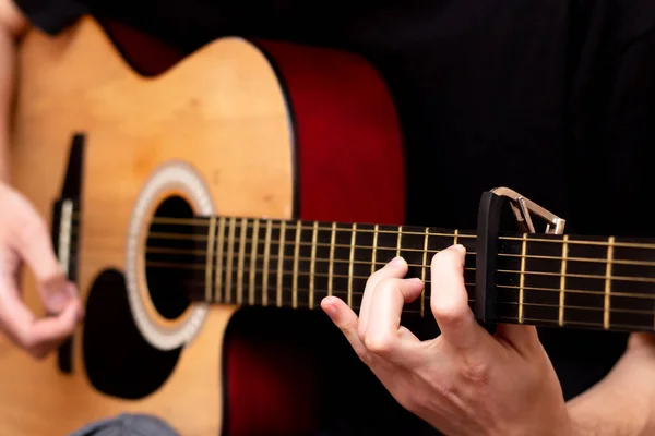 The guy plays the guitar. Capo on the guitar fretboard. Close plan. Wooden guitar.