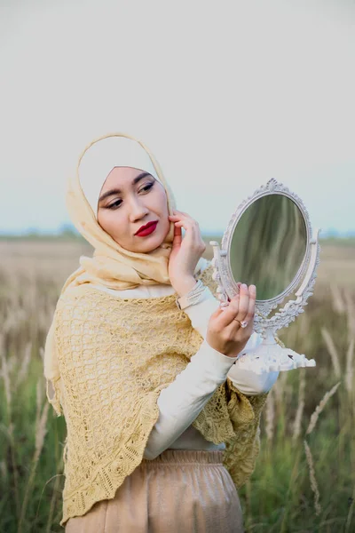 イスラム教徒の女性が畑の上に立ち 鏡を手にしている ベージュヒジャーブのムスリム女性 女性らしさ フェミニズム — ストック写真