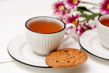 İki fincan çay ve yulaflı kurabiye. Pembe kasımpatılar. Kahvaltıda. Çay içiyorum. Beyaz tahta arkaplan.